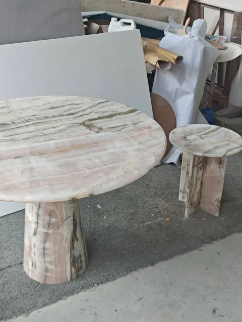 rose-red stone dining table, with a central pedestal base and banded onyx-like striping, in a workshop