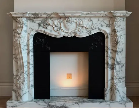 White Volakas marble fireplace surround, with fine veining and a reflective finish, in a furnished room