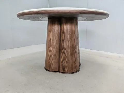 brown stone dining table, with a central pedestal base and a plain surface, against a pale background