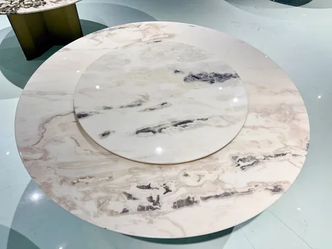 cream-beige stone dining table, with a round top and bold veining, in a showroom
