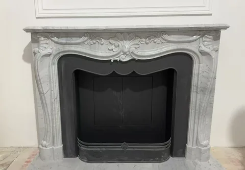 White Volakas marble fireplace surround, with carved scrollwork and fine veining, against a pale background