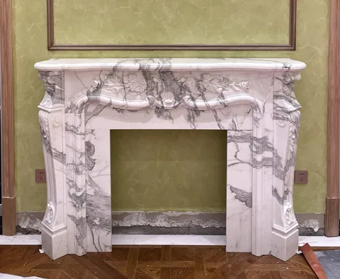 White Volakas marble fireplace surround, with carved scrollwork and bold veining, against a pale background