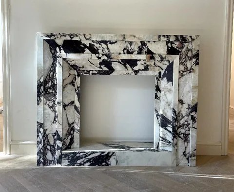 White Volakas marble fireplace surround, with stepped tiers and bold veining, against a pale background