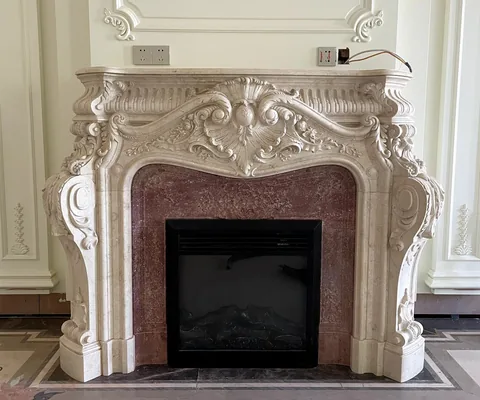 White Volakas marble fireplace surround, with carved scrollwork and cloudy mottling, in a furnished room