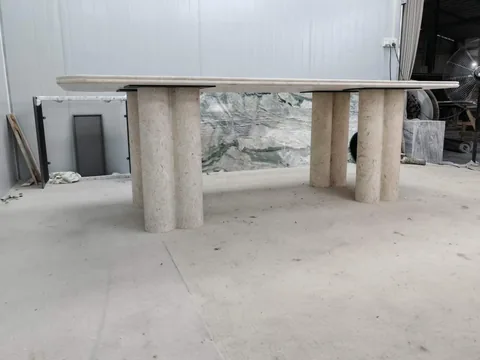 cream-beige stone dining table, with twin supporting bases and linear travertine grain, in a workshop