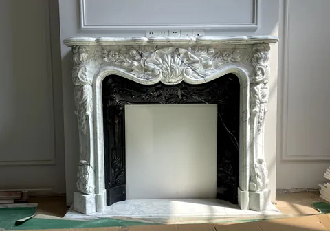 White Volakas marble fireplace surround, with carved scrollwork and fine veining, against a pale background