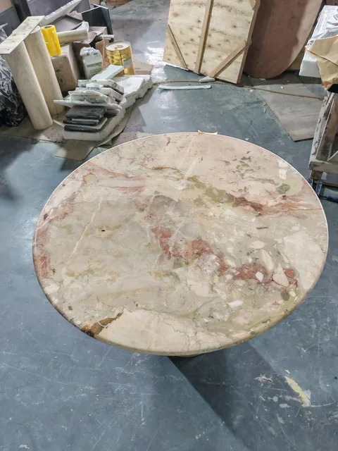 cream-beige stone coffee table, with a round top and cloudy mottling, in a workshop