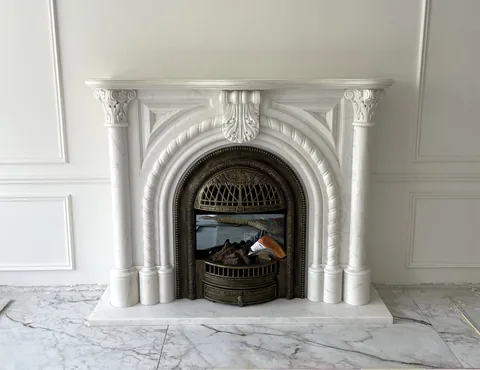 White Volakas marble fireplace surround, with fine veining, shown from a frontal view with workshop equipment nearby