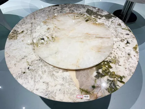 cream-beige stone dining table, with a round top and angular breccia fragments, in a showroom