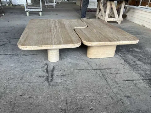 cream-beige stone coffee table, with a central pedestal base and linear travertine grain, in a workshop