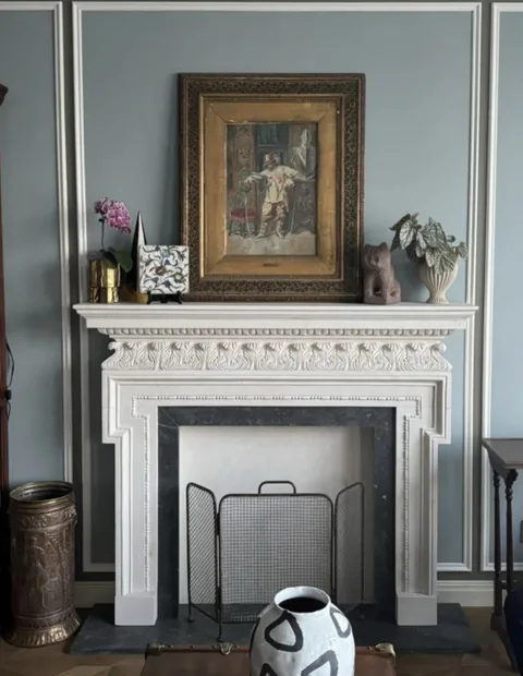 White Volakas marble fireplace surround, with stepped tiers and a plain surface, in a furnished room