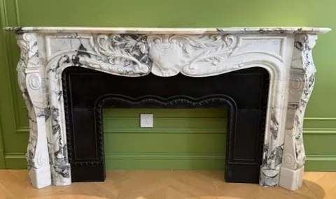 White Volakas marble fireplace surround, with carved scrollwork and bold veining, in a furnished room