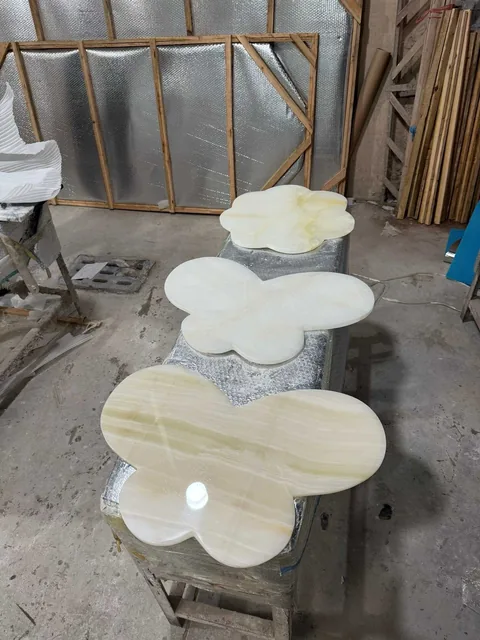 cream-beige stone coffee table, with an irregular organic edge and banded onyx-like striping, in a workshop