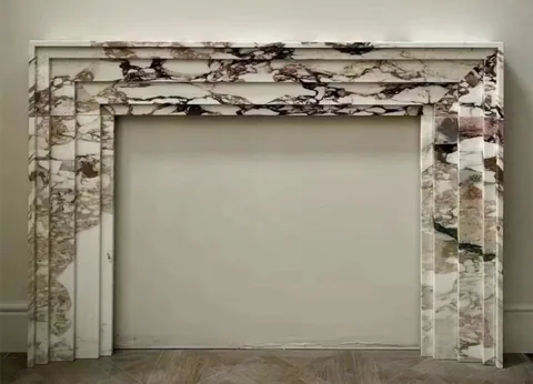 White Volakas marble fireplace surround, with stepped tiers and bold veining, against a pale background