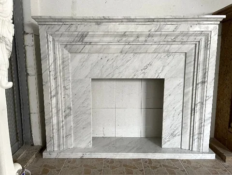 White Volakas marble fireplace surround, with stepped tiers and fine veining, against a pale background