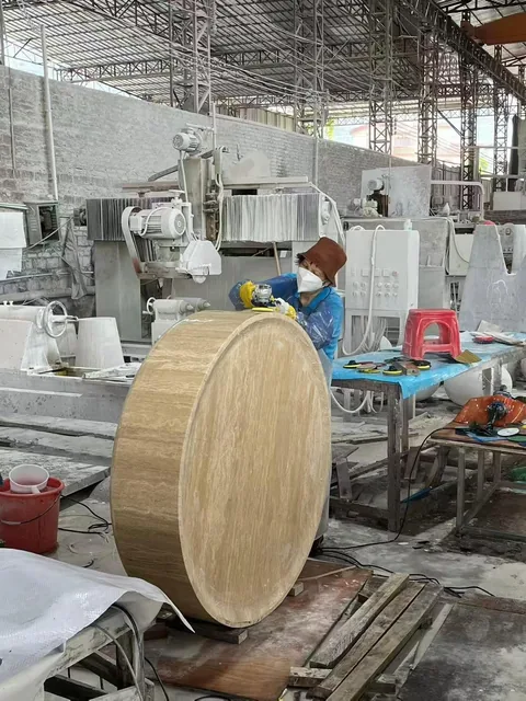 cream-beige stone dining table, with a round top and wood-like grain, in a workshop