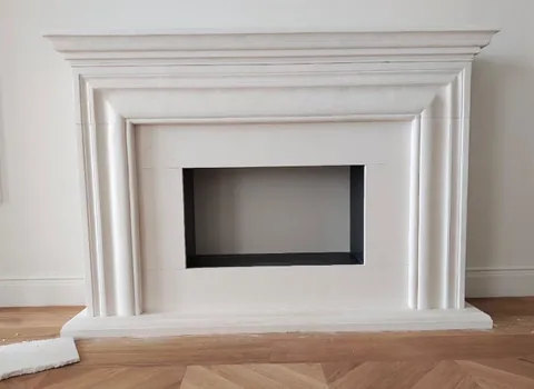 White Volakas marble fireplace surround, with stepped tiers and a plain surface, against a pale background