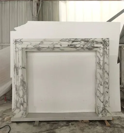 White Volakas marble fireplace surround, with stepped tiers and bold veining, in a workshop