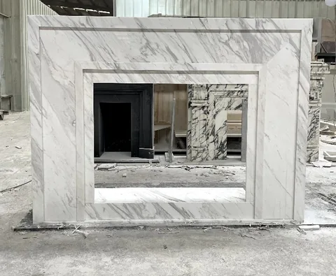 White Volakas marble fireplace surround, with fine veining, shown from a frontal view with workshop equipment nearby