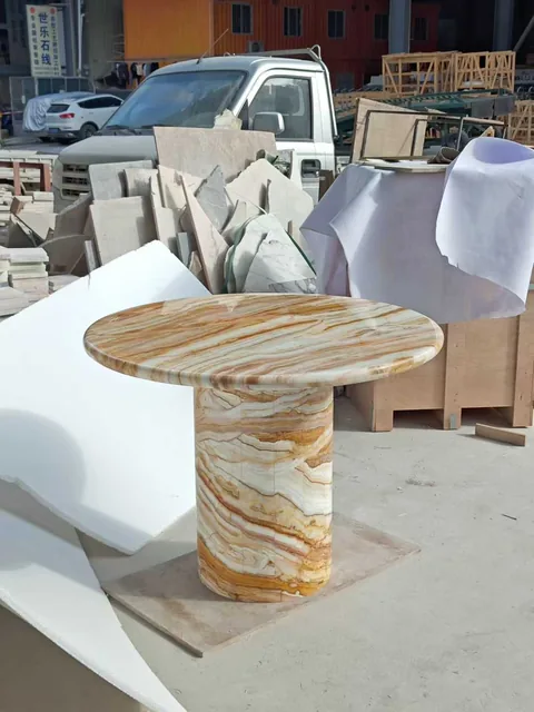 cream-beige stone side table, with a central pedestal base and banded onyx-like striping, in a workshop