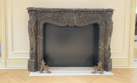 White Volakas marble fireplace surround, with carved scrollwork and fine veining, in a showroom