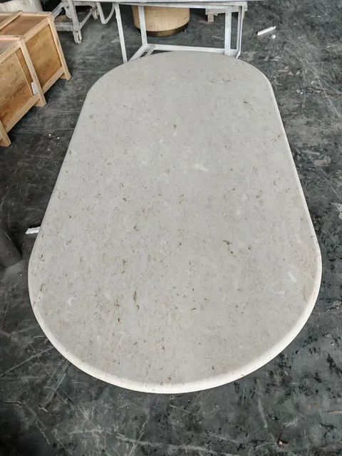 cream-beige stone dining table, with an oval top and cloudy mottling, in a workshop