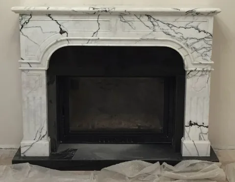 White Volakas marble fireplace surround, with an arched opening and bold veining, against a pale background