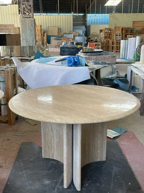 cream-beige stone dining table, with a round top and cloudy mottling, in a workshop