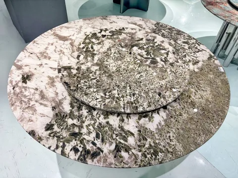 cream-beige stone dining table, with a round top and angular breccia fragments, in a showroom
