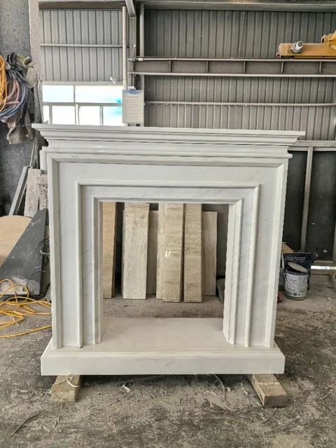 White Volakas marble fireplace surround, with fine veining and subtle pattern contrast and workshop equipment nearby