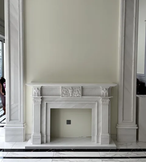 White Volakas marble fireplace surround, with a straight recessed opening and fine veining, in a furnished room