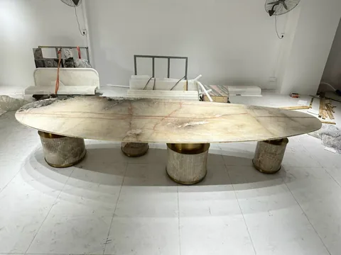 cream-beige stone dining table, with an oval top and fine veining, in a workshop