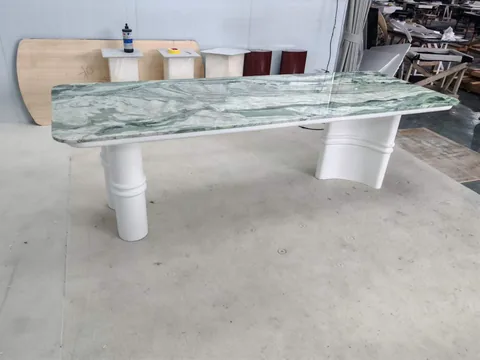 white stone dining table, with bold veining, showing a single main form with workshop equipment nearby