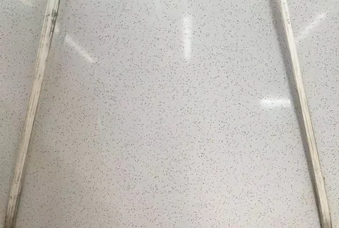white engineered stone slab, with a speckled texture and a reflective finish, against a pale background