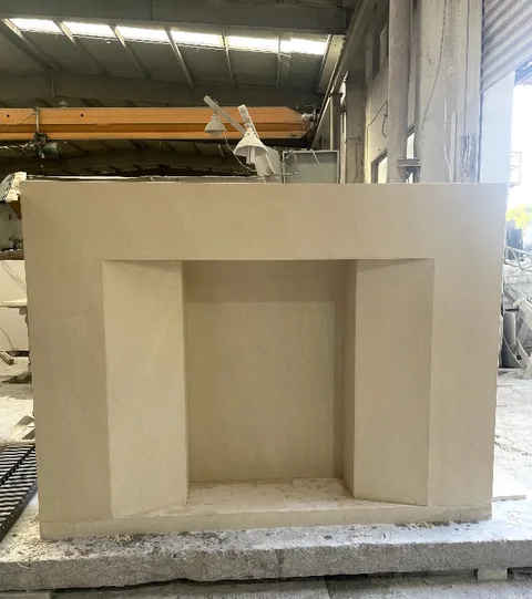 White Volakas marble fireplace surround, with a straight recessed opening and a plain surface, in a workshop