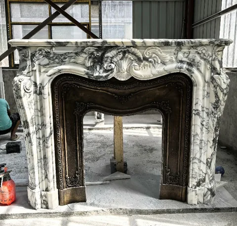 White Volakas marble fireplace surround, with carved scrollwork and bold veining, in a workshop