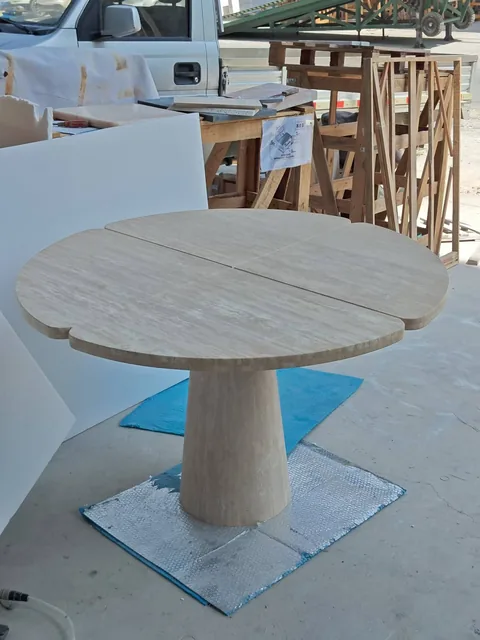 cream-beige stone dining table, with a central pedestal base and fine veining, in a workshop