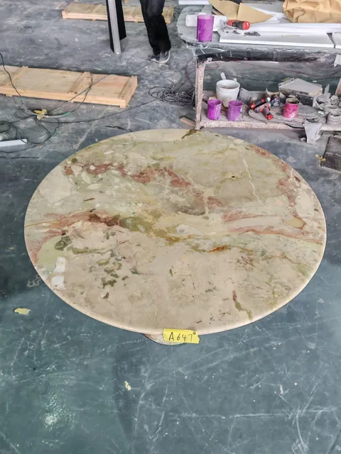 cream-beige stone dining table, with a round top and cloudy mottling, in a workshop