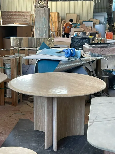 cream-beige stone dining table, with subtle pattern contrast and workshop equipment nearby