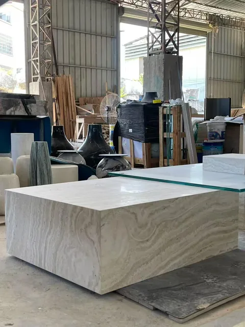 cream-beige stone coffee table, with a solid block base and banded onyx-like striping, in a workshop