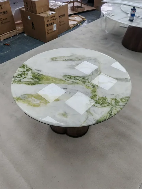 white stone dining table, with a round top and bold veining, in a workshop
