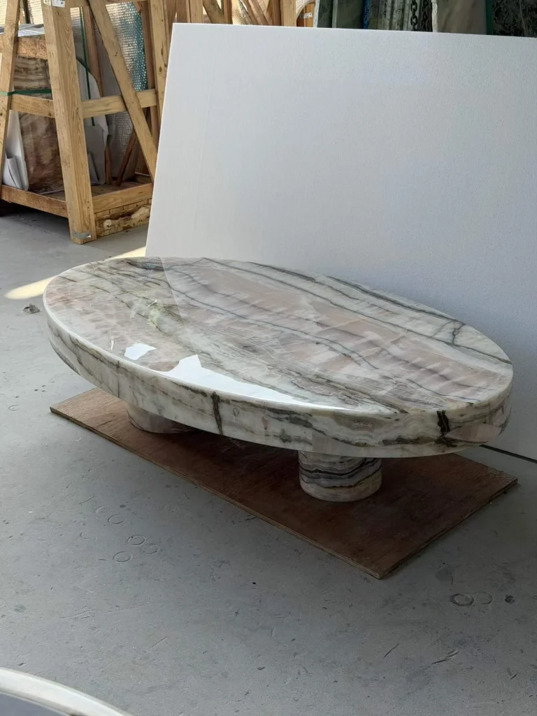 cream-beige stone coffee table, with twin supporting bases and banded onyx-like striping, in a workshop