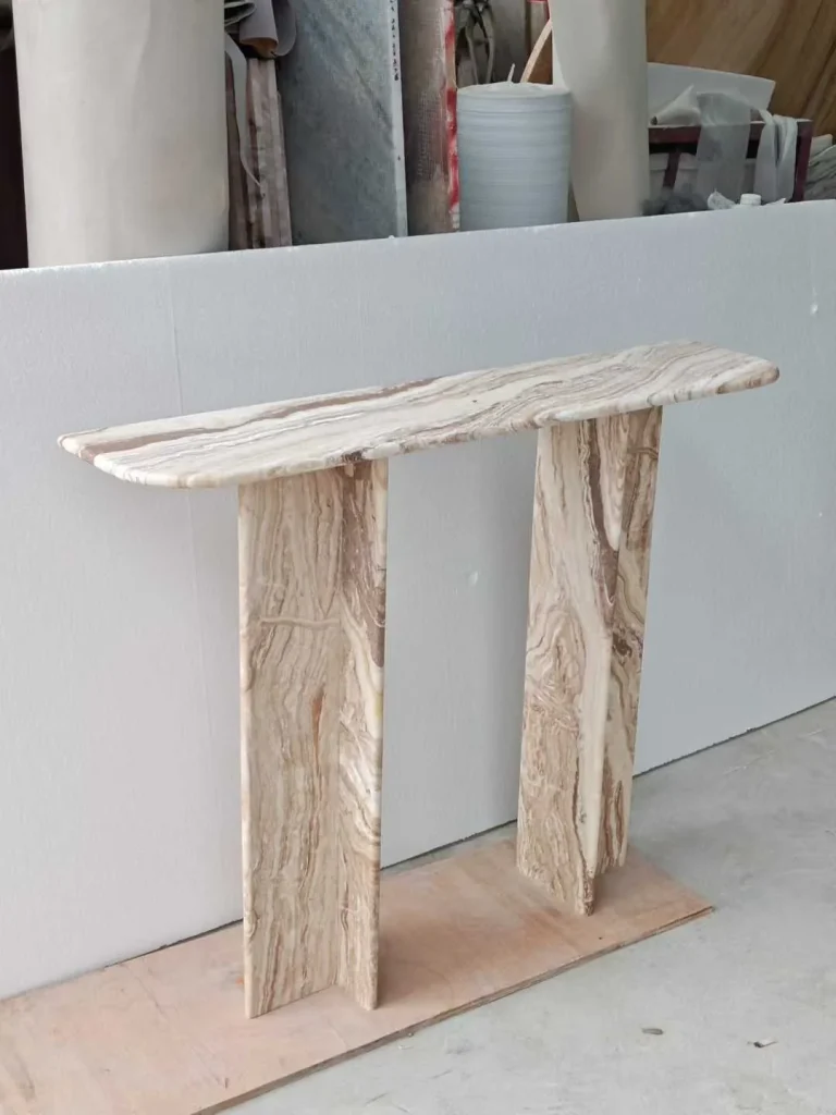 cream-beige stone console table, with twin supporting bases and banded onyx-like striping, in a workshop