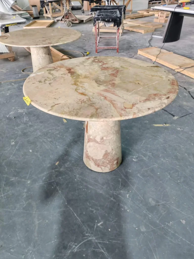 cream-beige stone dining table, with a central pedestal base and cloudy mottling, in a workshop