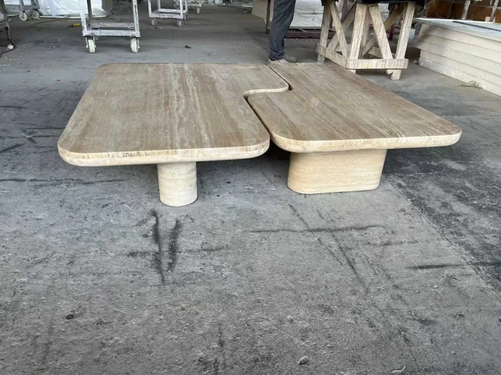 cream-beige stone coffee table, with a central pedestal base and linear travertine grain, in a workshop