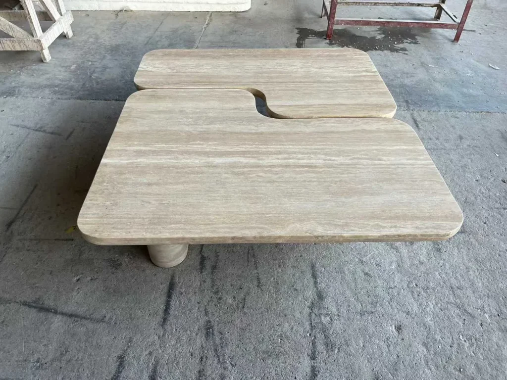 cream-beige stone coffee table, with a central pedestal base and linear travertine grain, in a workshop