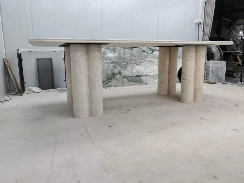 cream-beige stone dining table, with twin supporting bases and linear travertine grain, in a workshop