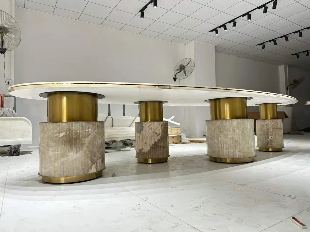 cream-beige stone dining table, with an oval top and linear travertine grain, in a workshop