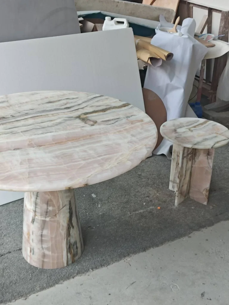 rose-red stone dining table, with a central pedestal base and banded onyx-like striping, in a workshop