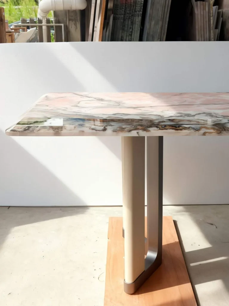rose-red stone dining table, with a central pedestal base and banded onyx-like striping, against a pale background